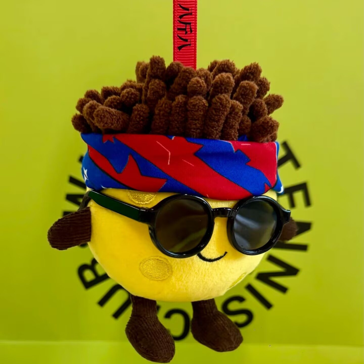 Plush toy with sunglasses and a colorful headband on a green background