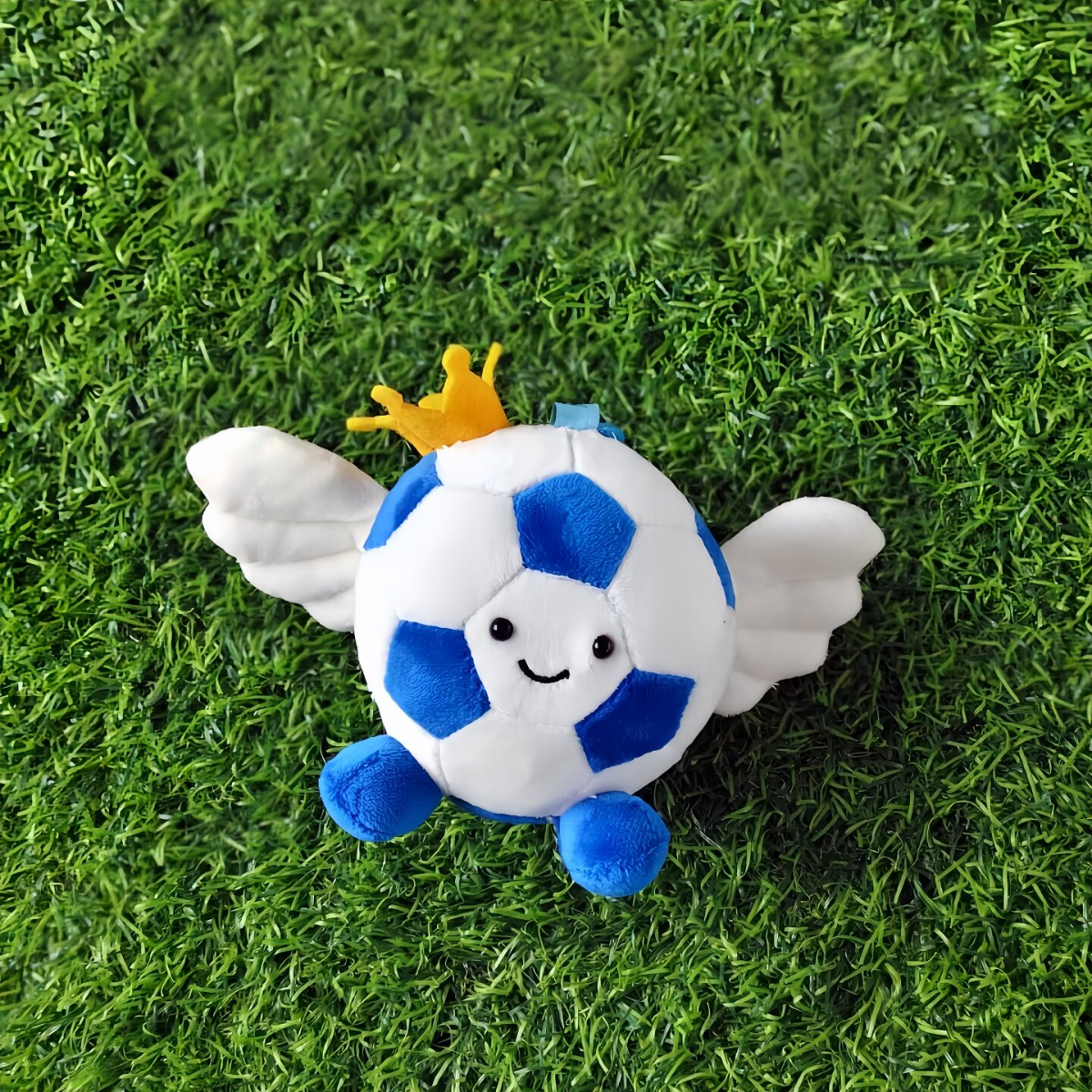 Plush toy resembling a soccer ball with wings and a crown on grass